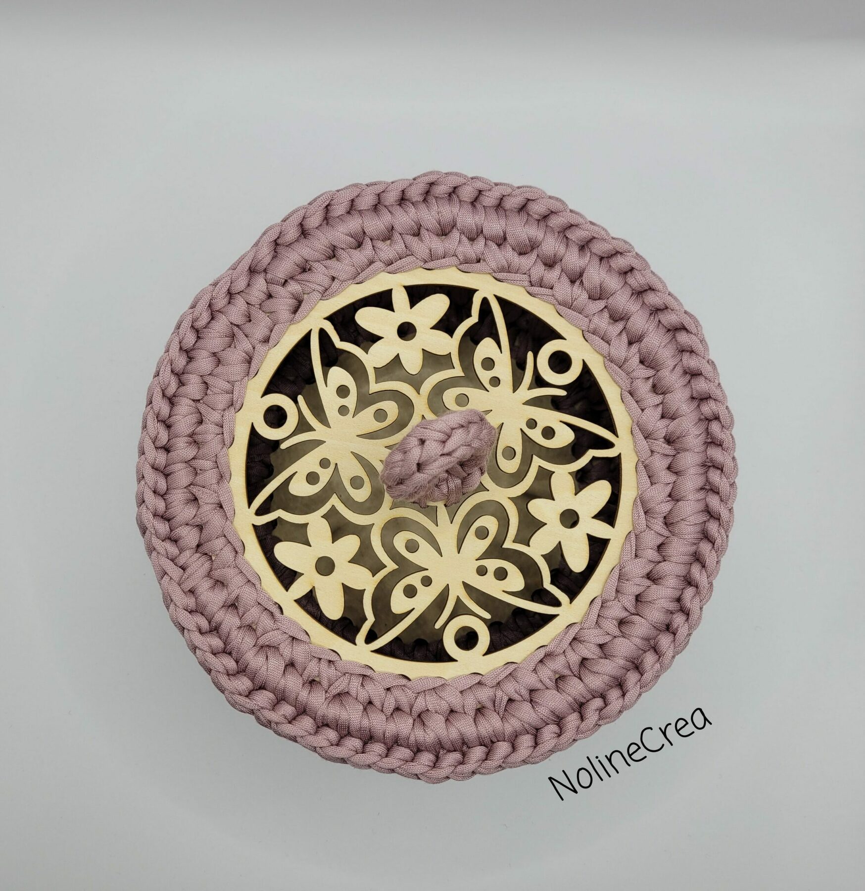 vue plongé d'une base en bois sculpté avec des papillons et fleurs, un fil rose est crocheté tout autour