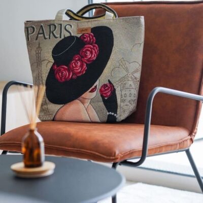 Tote bag artisanal avec motif jacquard Paris, avecune femme en chapeau noir orné de roses rouge posé sur un fauteuil en cuir marron