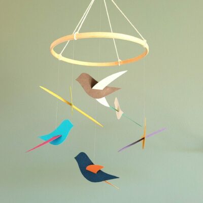 Mobile pour bébé avec oiseaux colorés en papier recyclé suspendus à un cercle en bois clair, fait main en Bretagne par La Fabrique en Papier. Déco écoresponsable pour chambre d’enfant.