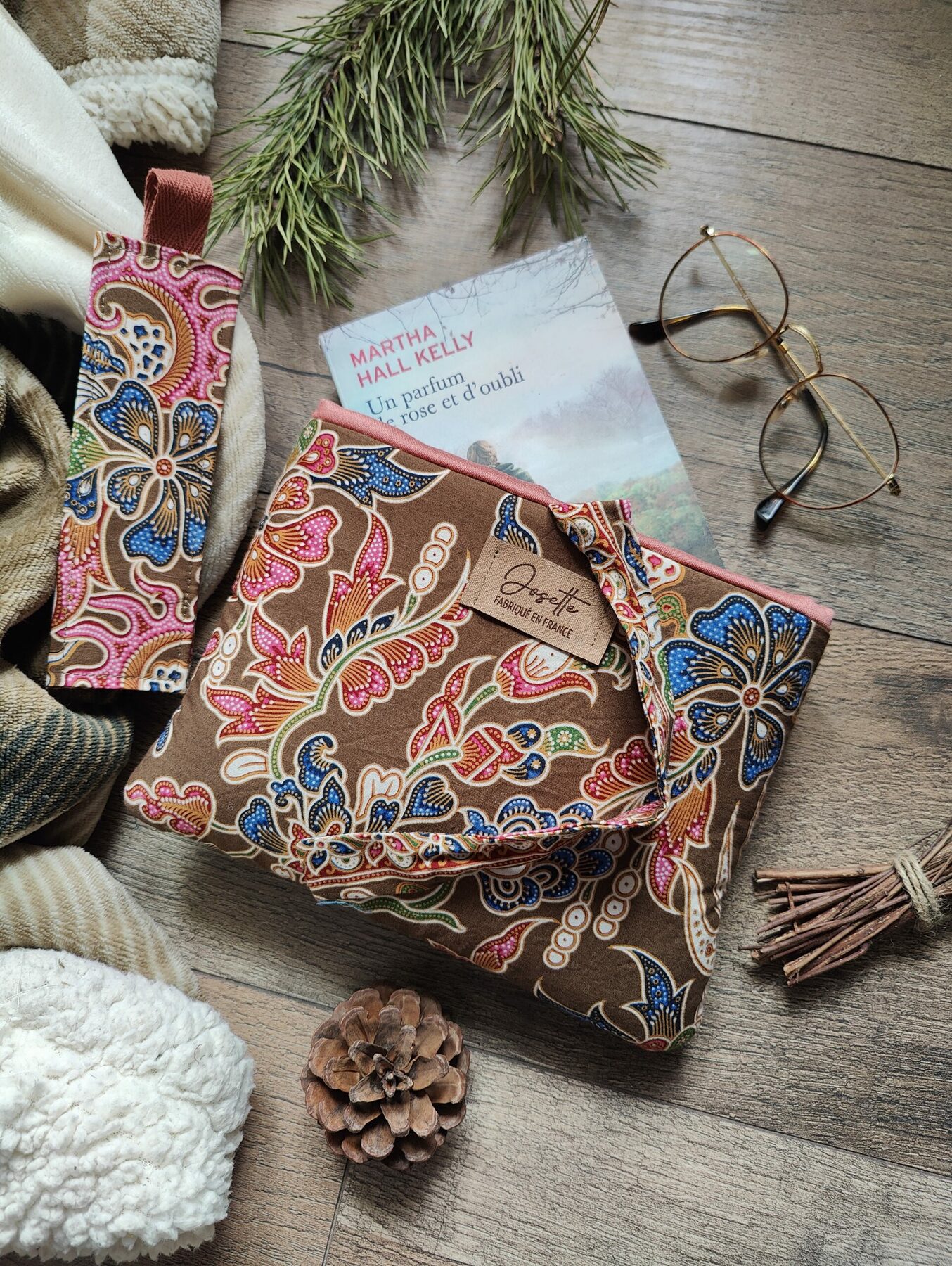 Pochette et marque-page assorti en tissu fleuri marron posés sur un parquet avec un livre et des lunettes.