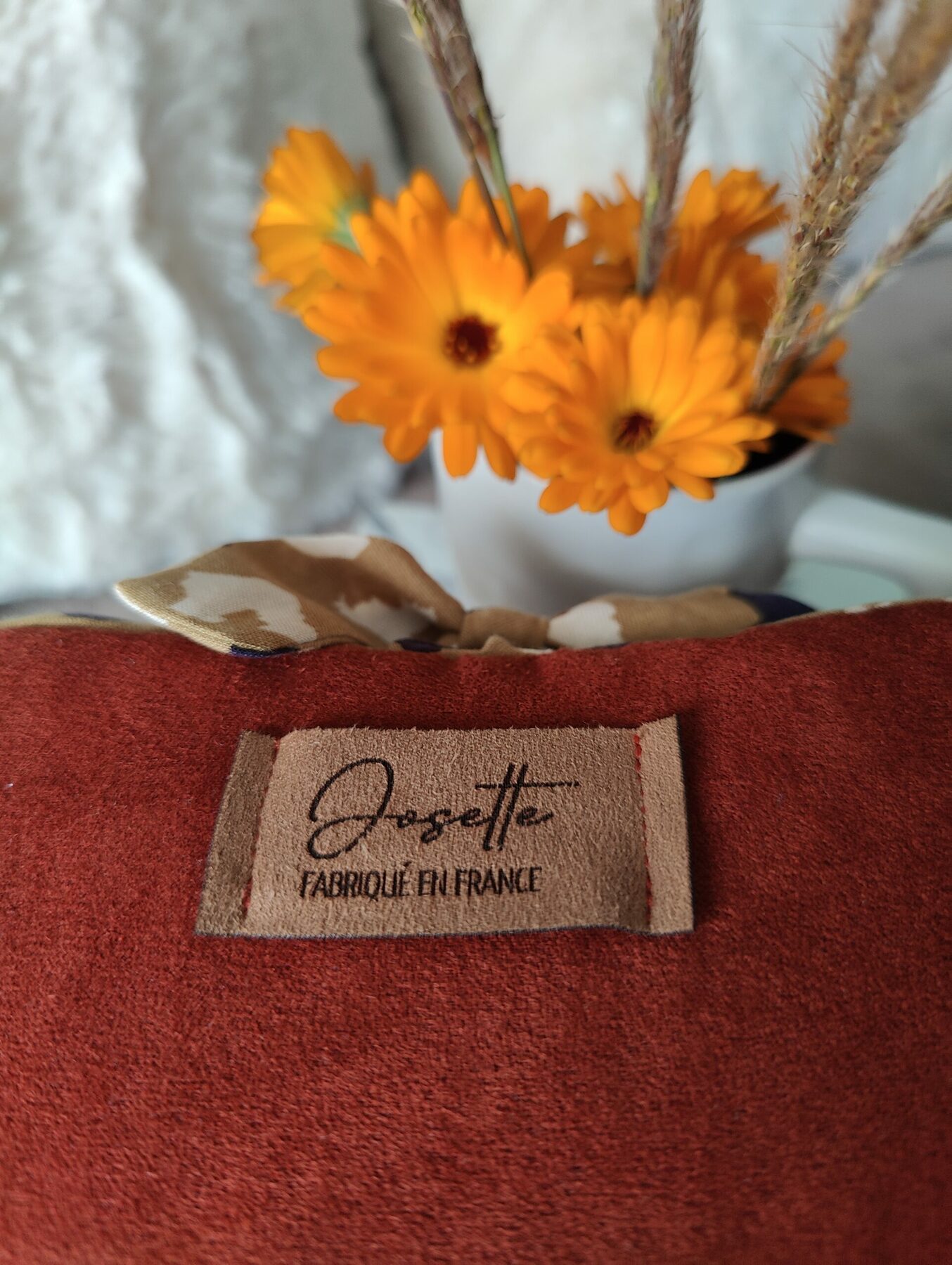 Gros plan sur le tissu couleur rouille d’une pochette livre avec l’étiquette Atelier Josette.