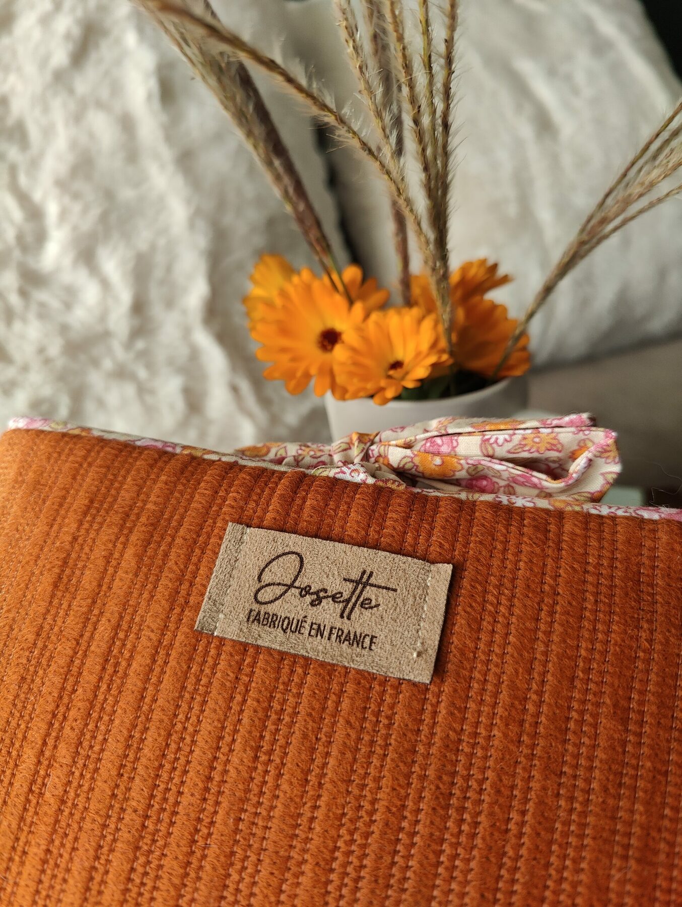 Gros plan sur le tissu orangé d’une pochette liseuse avec l’étiquette Atelier Josette.