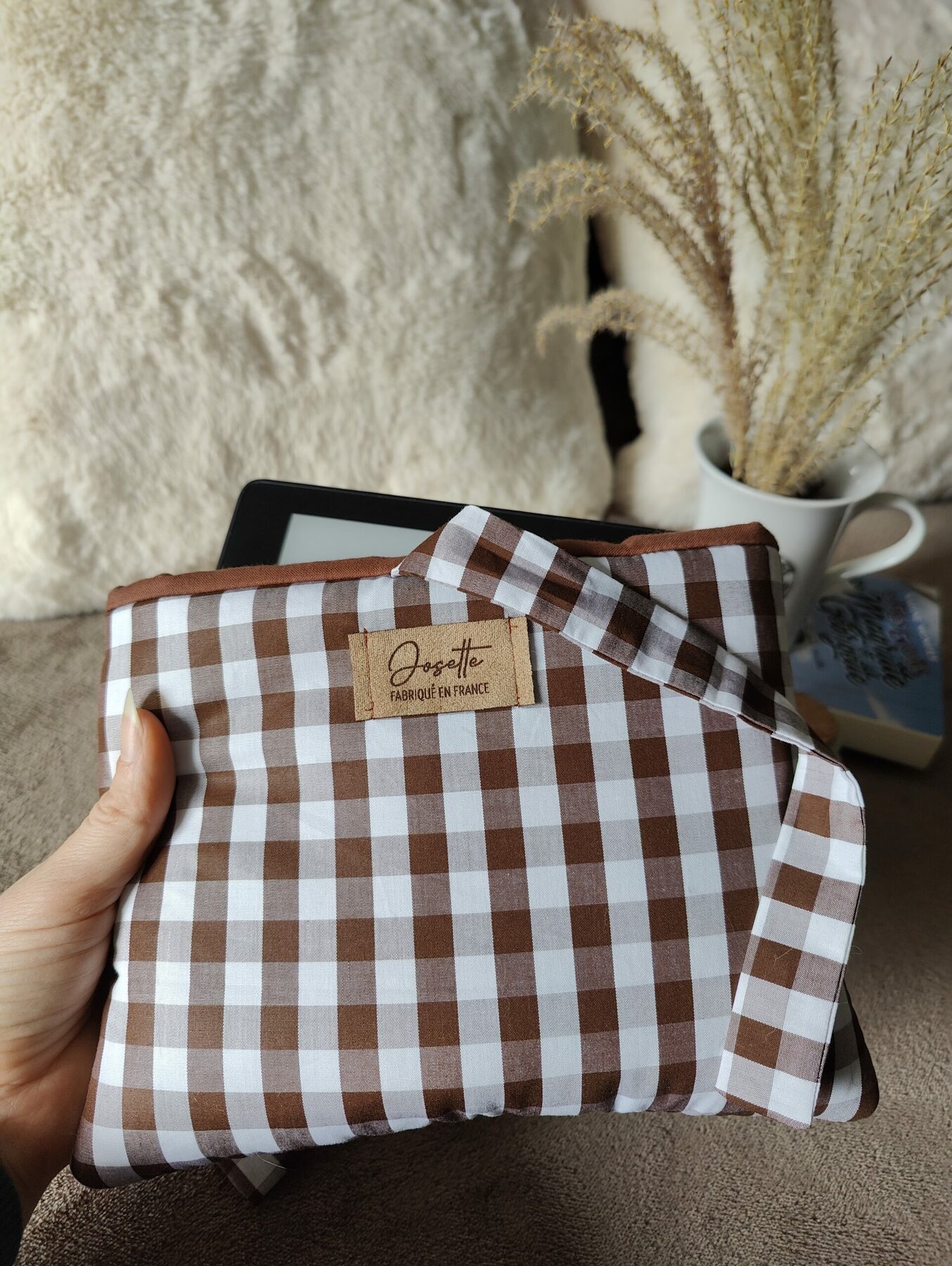 Pochette à carreaux contenant une liseuse, présentée sur le même fond cosy.
