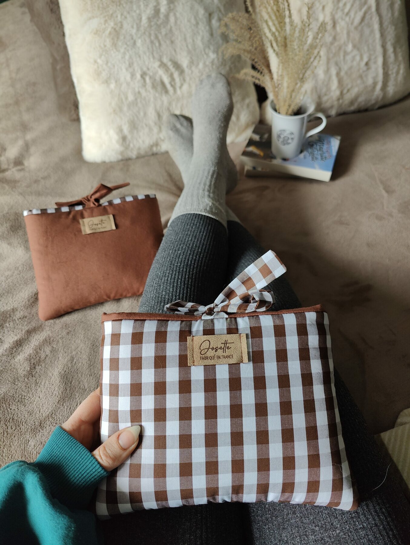 Pochette à carreaux tenue sur les jambes, la pochette marron visible à côté, scène d’usage.