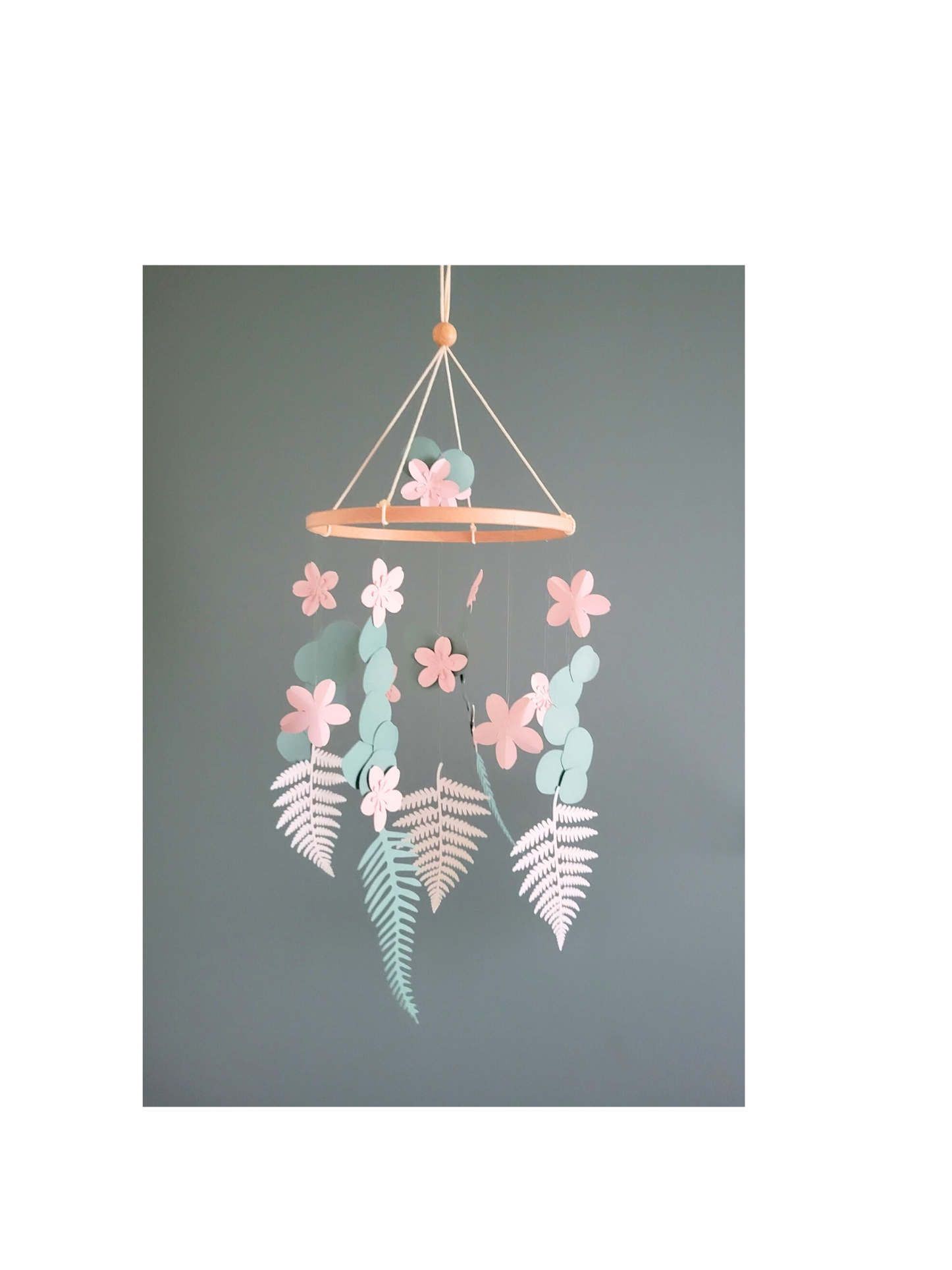 Mobile bébé fleurs de cerisier et eucalyptus en papier recyclé suspendu sur fond gris.