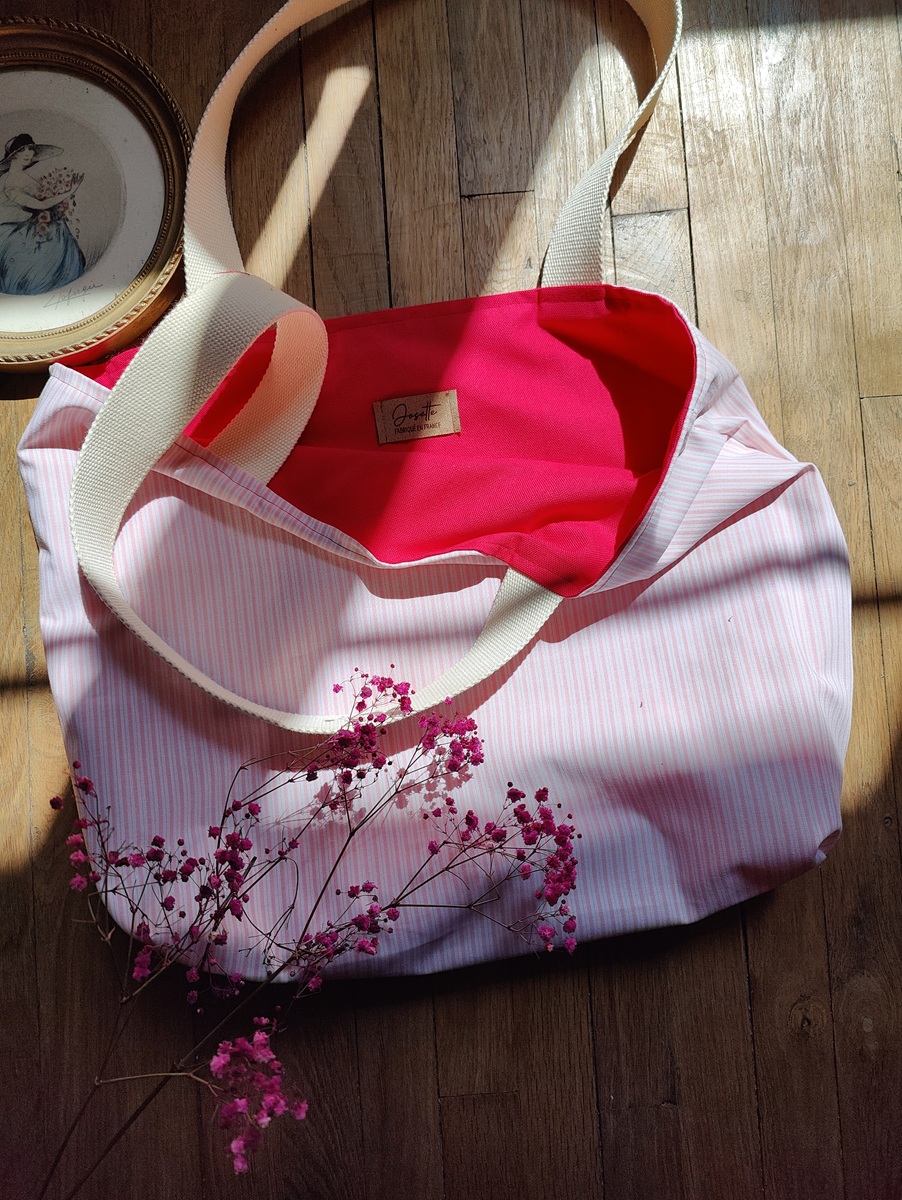 Tote bag réversible upcyclé posé sur un sol en bois, côté rayé blanc et rose visible avec intérieur fuchsia, décoré de gypsophiles roses.