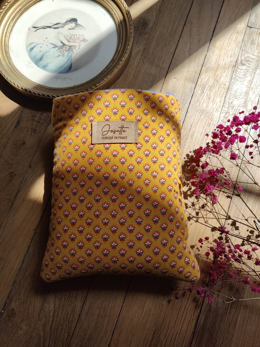 Pochette à livre upcyclée en serviette de table à motifs fleurs , posée sur une table en bois, avec un cadre doré et des fleurs roses en décoration.