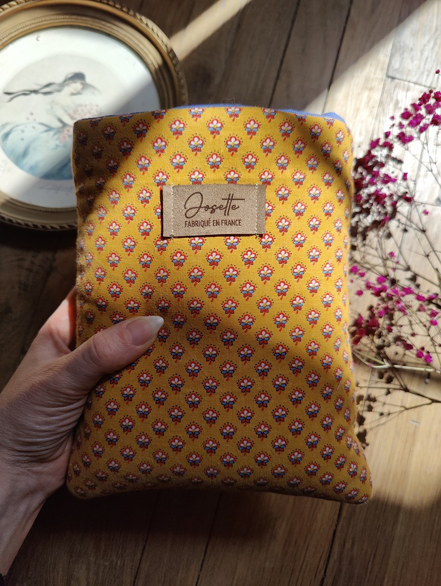 Pochette à livre upcyclée tenue dans une main, côté motifs fleurs sur fond jaune visible, montrant sa taille compacte.