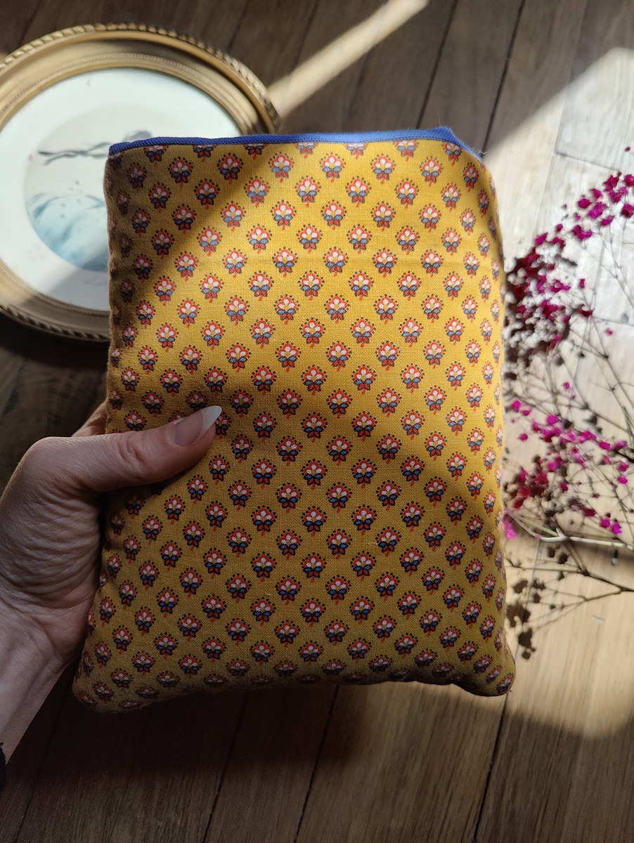 Pochette à livre upcyclée tenue dans une main, côté dos en motifs fleurs sur fond jaune visible, montrant la continuité du tissu.
