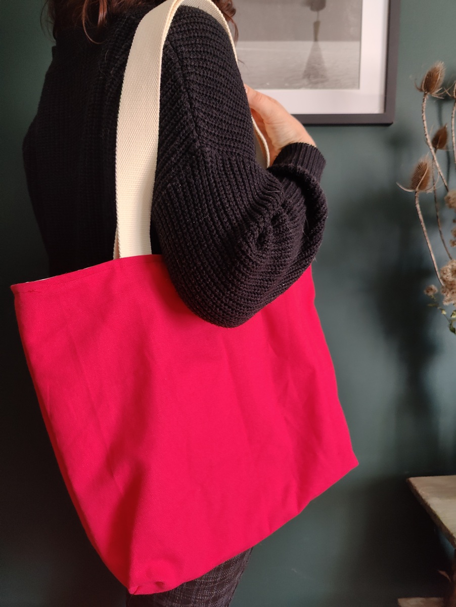 Tote bag réversible upcyclé porté à l’épaule, côté fuchsia, montrant son tombant naturel et ses anses en coton.