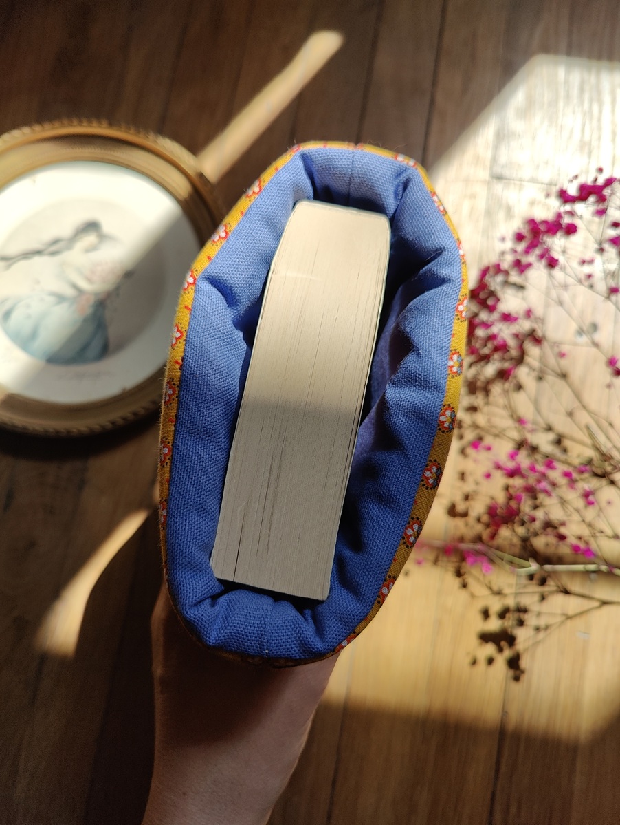 Vue du dessus d’une pochette à livre upcyclée, montrant l’ouverture et l’intérieur bleu contrastant avec les motifs fleurs sur fond jaune.