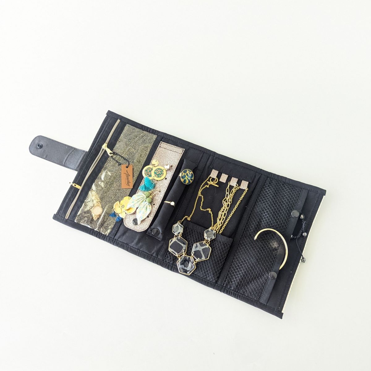 Pochette à bijoux ouverte à plat, vue d'ensemble — intérieur coton noir avec filet mesh, supports colliers et bijoux fantaisie