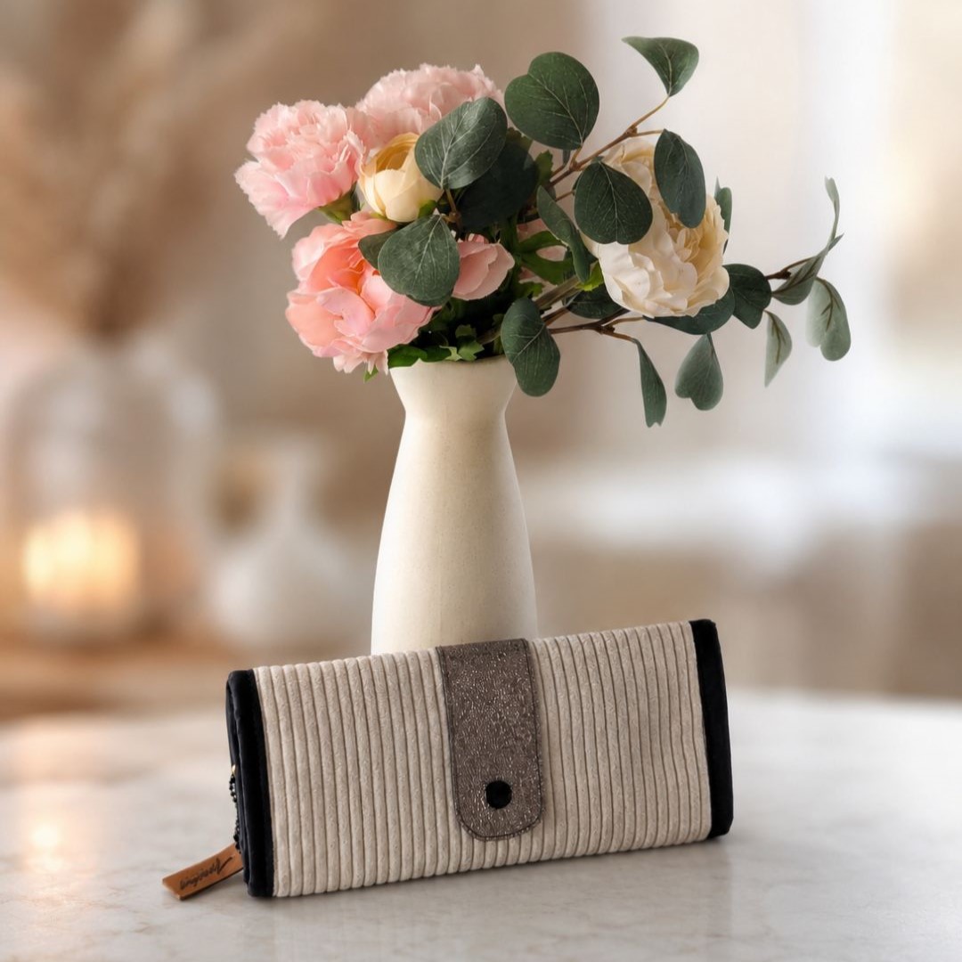Pochette à bijoux de voyage en velours côtelé écru posée sur une table, mise en scène avec un bouquet de roses — création artisanale Ineden Couture