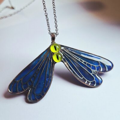Pendentif artisanal sculpté en forme de papillon par l'artiste Yulia Tauritari, conçu en acier inoxydable argenté et résine époxy. Il se distingue par de grands yeux verts expressifs, des ailes aux nuances de bleu nacré et une incroyable propriété luminescente qui brille doucement dans l'obscurité. 6 x 7 cm Acier inoxydable et résine époxy Argenté, bleu nacré, vert Écrin soigné et écologique, prêt à offrir Effet luminescent dans le noir, fabrication artisanale entièrement fait main, pièce unique signée Fantasy, art nouveau, art déco, gothique, féérique, elfique