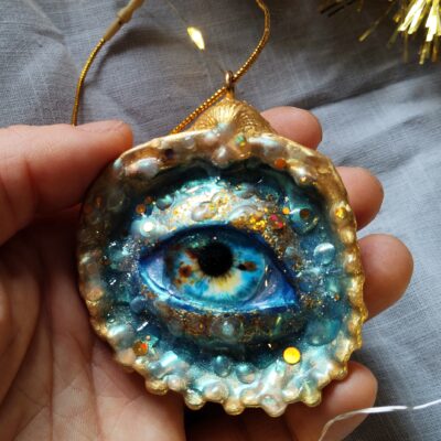 Décoration de Noël en forme de coquillage ornée d’un œil bleu et doré. Dimensions : 8 x 10 cm Matériaux : coquillage naturel, verre, résine époxy, pâte polymère Couleurs : bleu, turquoise, or, doré Livré dans une boîte cadeau soignée avec une petite attention surprise. Les détails brillent et réagissent sous la lumière UV. Gothique, féerique, fantastique, cabinet de curiosités, mystique, witchy.