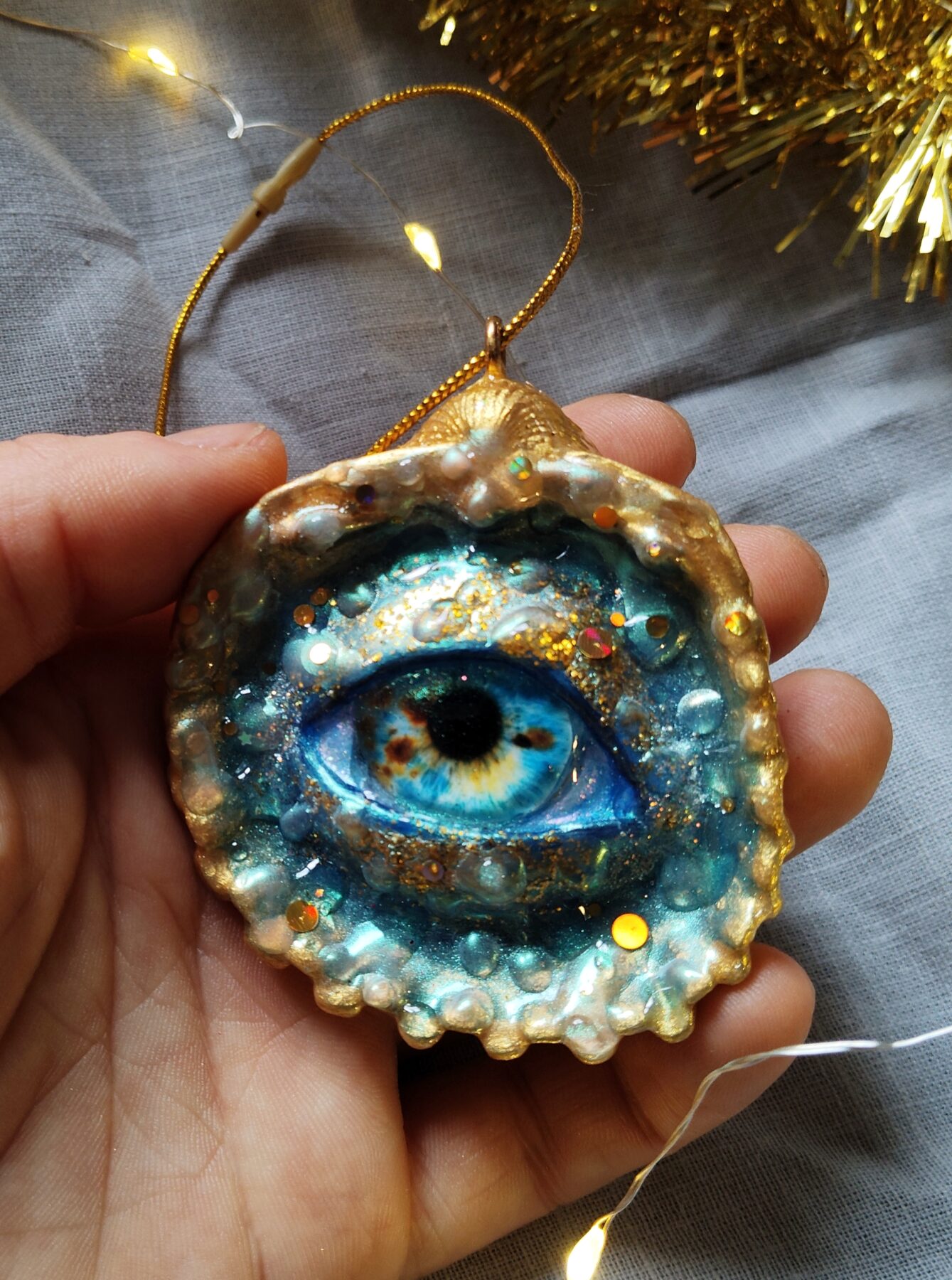 Décoration de Noël en forme de coquillage ornée d’un œil bleu et doré. Dimensions : 8 x 10 cm Matériaux : coquillage naturel, verre, résine époxy, pâte polymère Couleurs : bleu, turquoise, or, doré Livré dans une boîte cadeau soignée avec une petite attention surprise. Les détails brillent et réagissent sous la lumière UV. Gothique, féerique, fantastique, cabinet de curiosités, mystique, witchy.